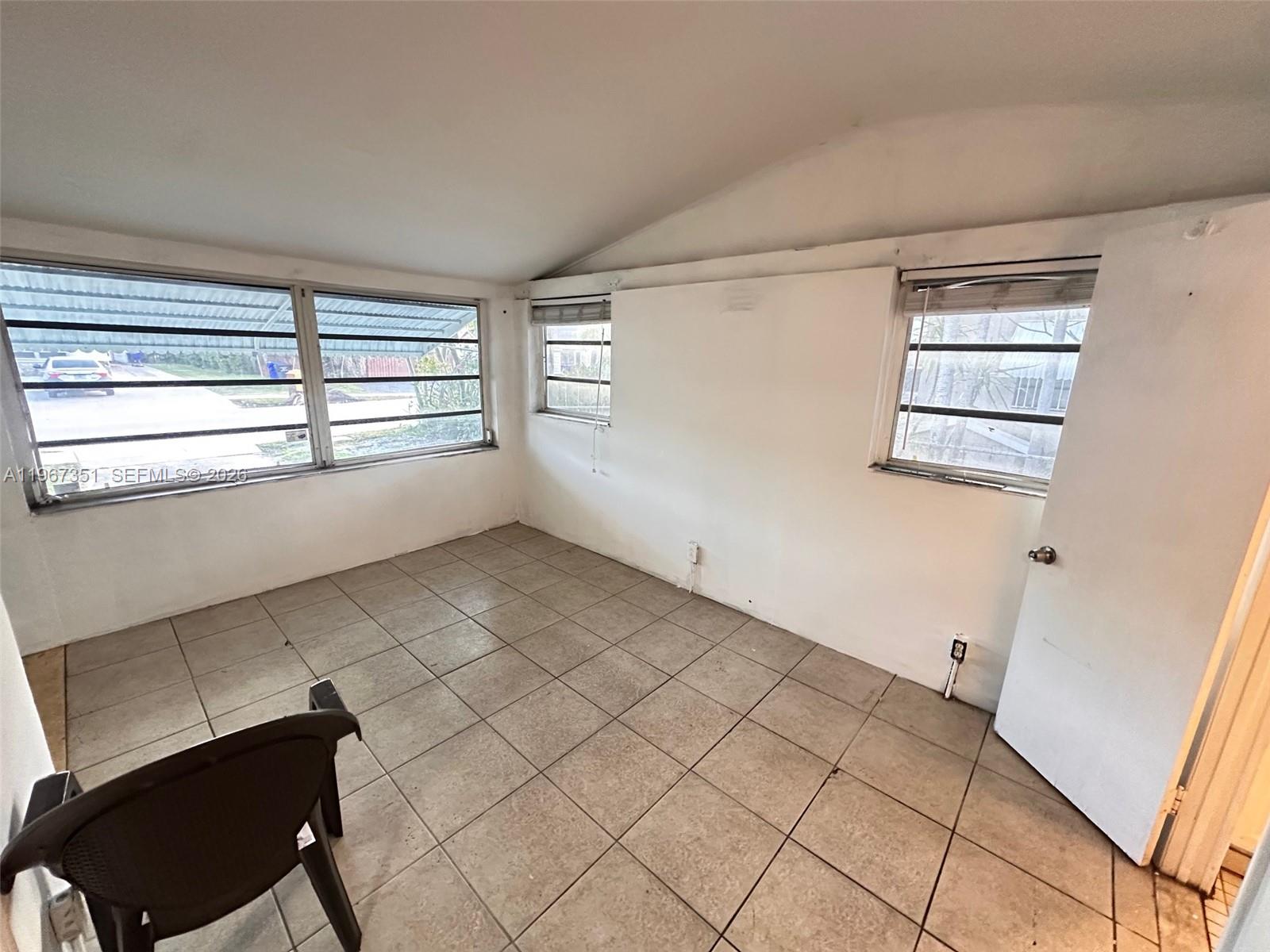An empty room features white walls, tiled flooring, and multiple windows with horizontal blinds — 1829 Harding St, Hollywood FL 33020, HOLLYWOOD, FL