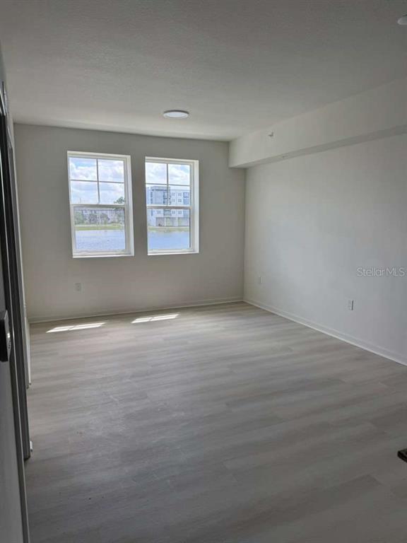 An empty room with light wood-look flooring and two windows overlooking a body of water — 5579 MILLENIA PARK BOULEVARD UNIT 203, ORLANDO, FL