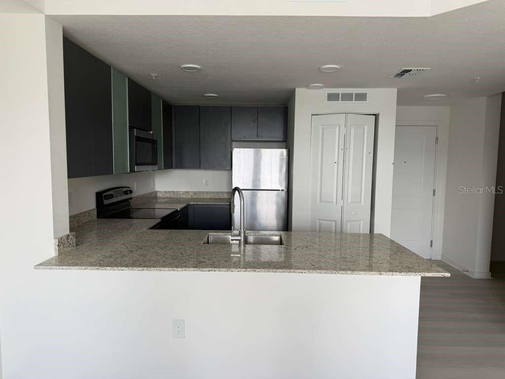 A kitchen features dark cabinets, granite countertops, stainless steel appliances, and a breakfast bar — 5579 MILLENIA PARK BOULEVARD UNIT 203, ORLANDO, FL