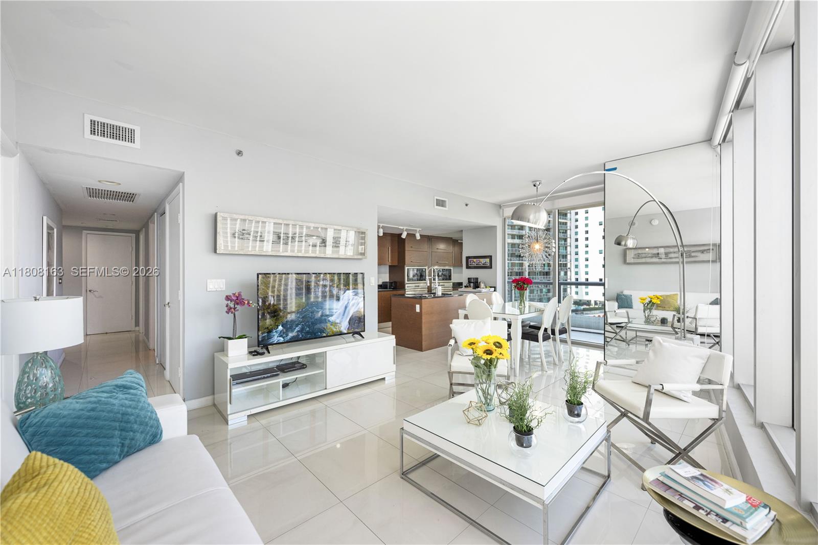 A modern living room features white tile floors, a television, and an open kitchen area — 485 Brickell Ave # 1604, Miami FL 33131, MIAMI, FL