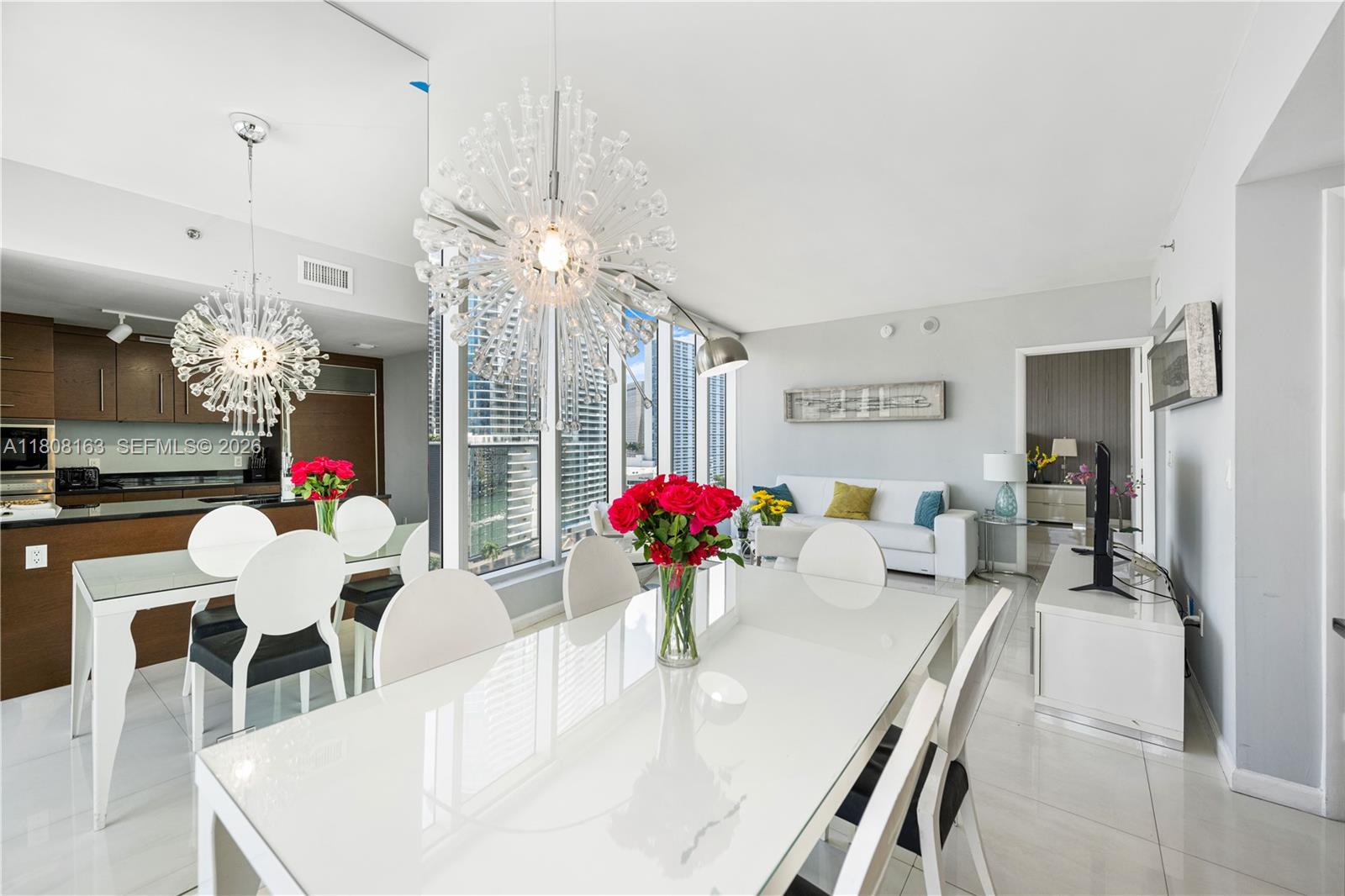 A modern dining area with a white table and chairs sits before a city view — 485 Brickell Ave # 1604, Miami FL 33131, MIAMI, FL