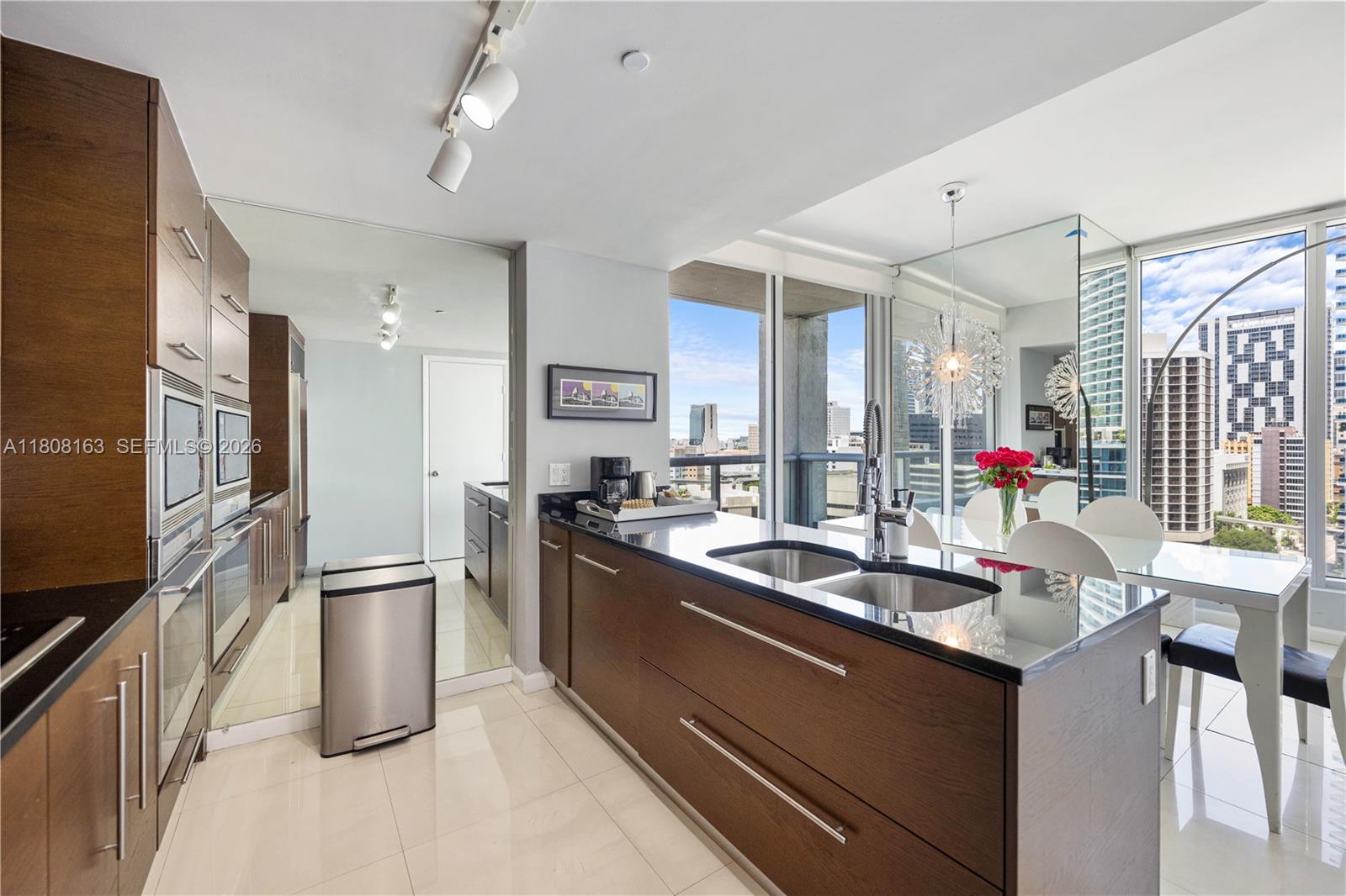 A modern kitchen features dark wood cabinetry, black countertops, stainless steel appliances, and city views — 485 Brickell Ave # 1604, Miami FL 33131, MIAMI, FL
