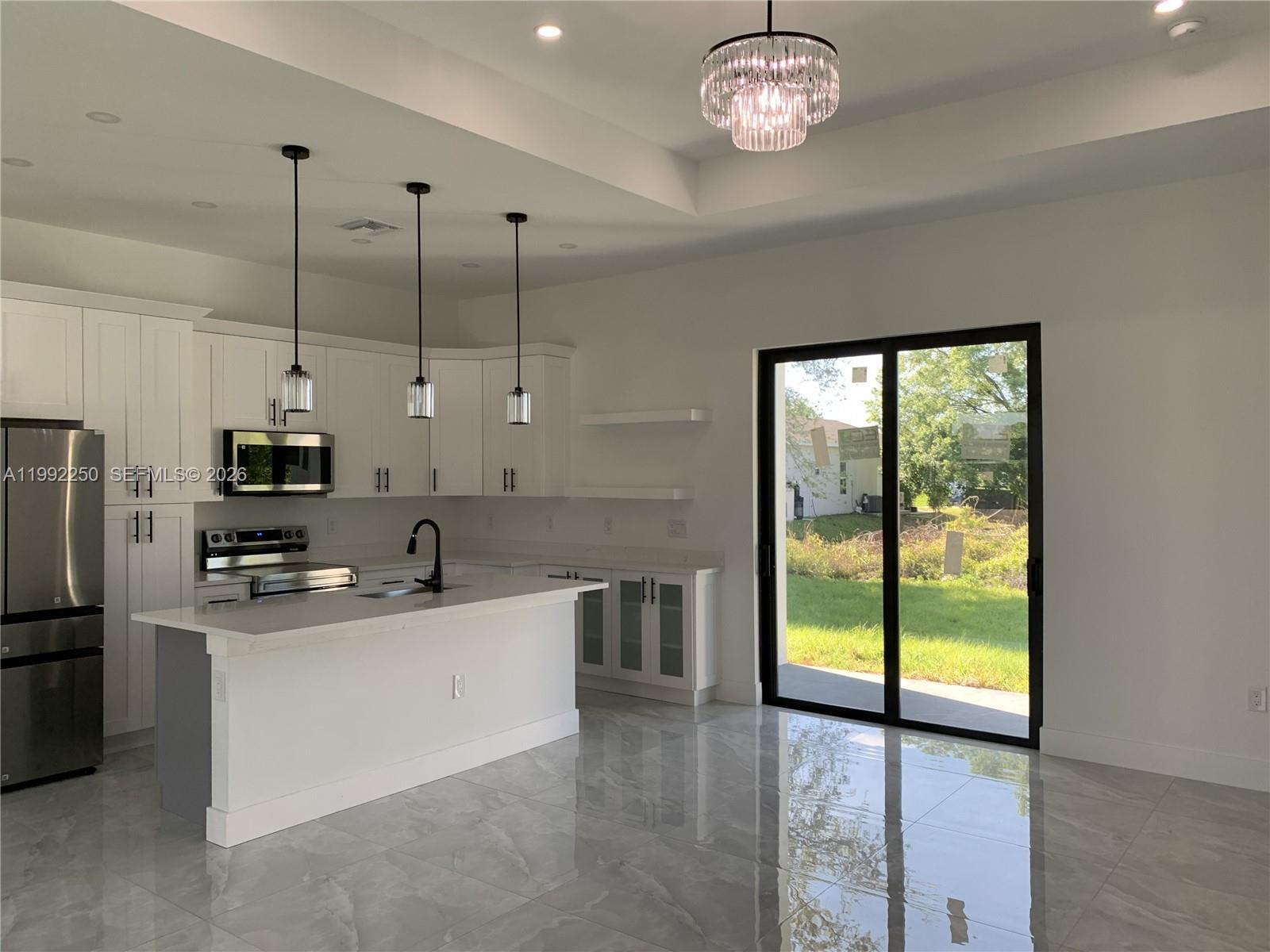 A modern kitchen features white cabinetry, a central island, and sliding glass doors to outdoors — 442 Redwing St, Lehigh Acres FL 33974, LEHIGH ACRES, FL