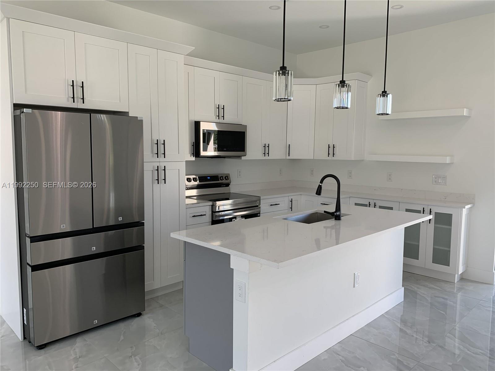 A modern kitchen features white cabinetry, stainless steel appliances, a center island, and pendant lighting — 442 Redwing St, Lehigh Acres FL 33974, LEHIGH ACRES, FL