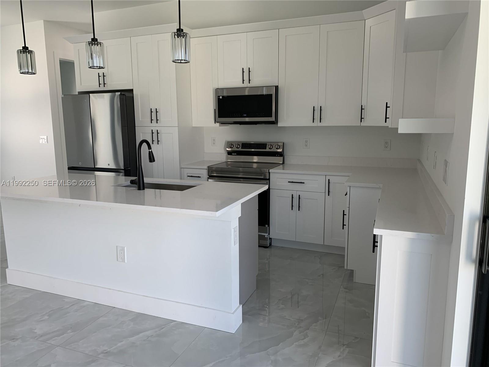 A modern kitchen features white cabinets, stainless steel appliances, a quartz island, and tiled floors — 442 Redwing St, Lehigh Acres FL 33974, LEHIGH ACRES, FL