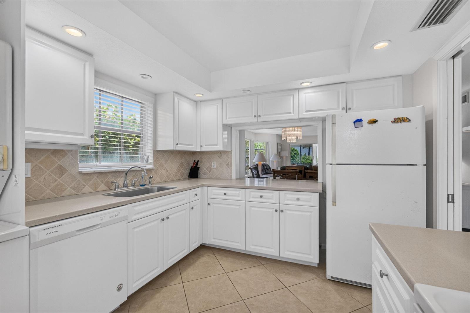 A white kitchen features light countertops, tile backsplash, tile flooring, and a pass-through window — 120 Celestial Way # 114, Juno Beach FL 33408, JUNO BEACH, FL