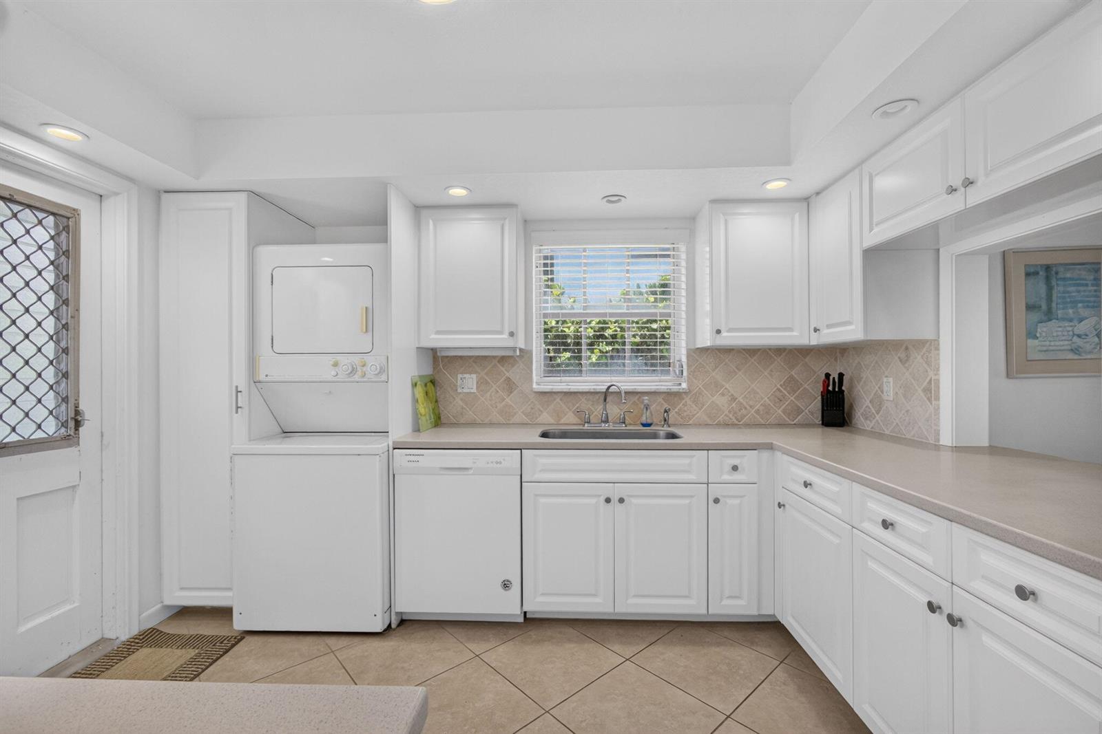A kitchen features white cabinets, a stacked washer and dryer, and beige tile flooring — 120 Celestial Way # 114, Juno Beach FL 33408, JUNO BEACH, FL