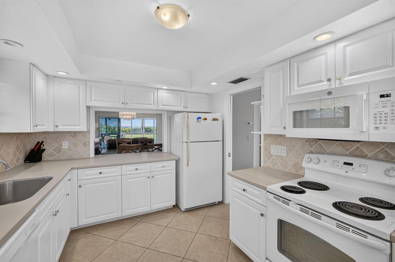 A kitchen with white cabinets, light countertops, tile flooring, and a pass-through window to outdoors — 120 Celestial Way # 114, Juno Beach FL 33408, JUNO BEACH, FL
