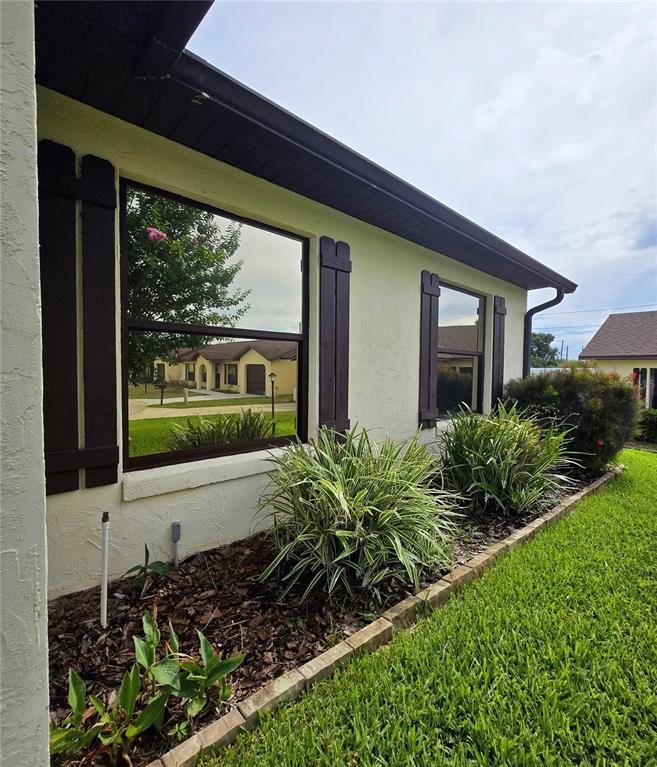 The exterior of a house features stucco walls, dark shutters, and a landscaped garden bed — 1980 TRINITY CIRCLE, HAINES CITY, FL