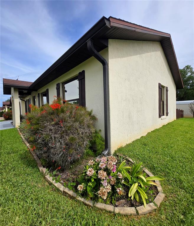 The exterior of a light-colored house features a landscaped garden bed with flowering shrubs — 1980 TRINITY CIRCLE, HAINES CITY, FL