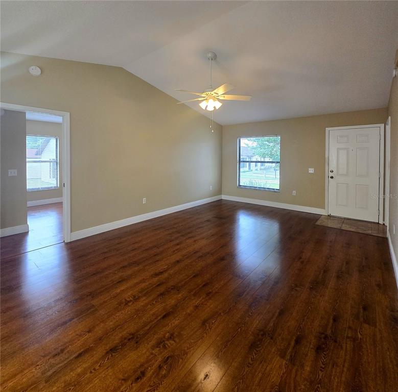 An empty living room features dark wood-look flooring, a vaulted ceiling, and a ceiling fan — 1980 TRINITY CIRCLE, HAINES CITY, FL