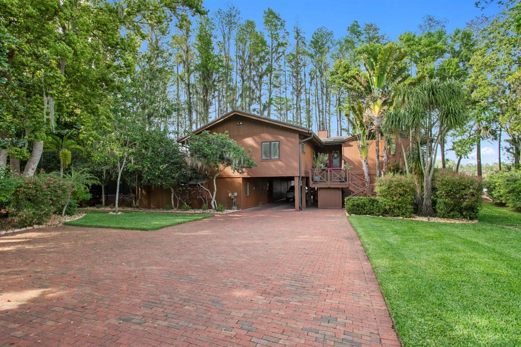 A two-story brown wood-sided house features a brick driveway and a covered ground-level parking area — 8817 ROBERTS ROAD, ODESSA, FL