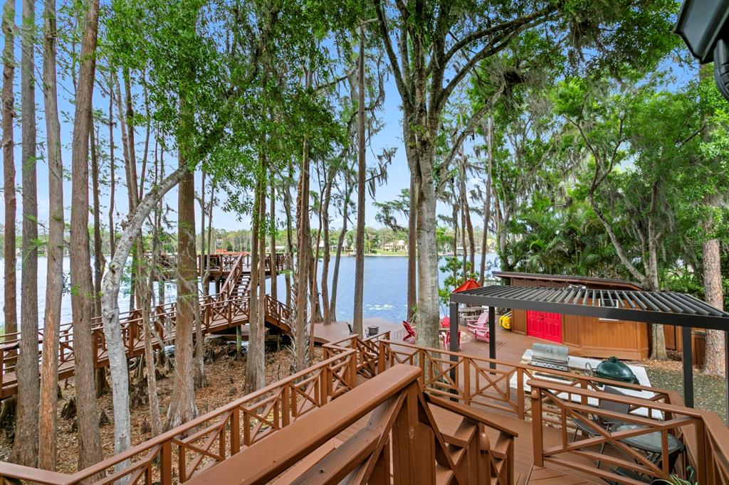 A multi-level wooden deck overlooks a lake with a pergola, outdoor grill, and surrounding trees — 8817 ROBERTS ROAD, ODESSA, FL