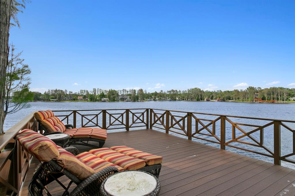 A wooden deck with lounge chairs overlooks a lake under a clear blue sky — 8817 ROBERTS ROAD, ODESSA, FL