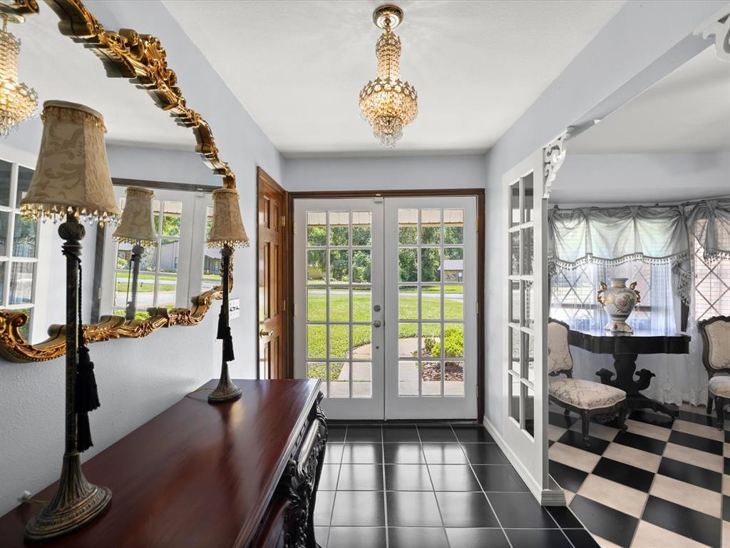 A foyer features black tile flooring, a crystal chandelier, a wooden console table, and mirrors — 10721 SKYHAWK DRIVE, NEW PORT RICHEY, FL