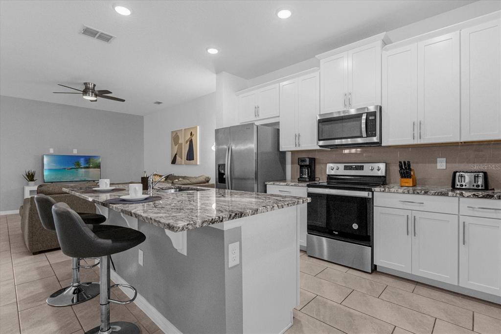 A modern kitchen features white cabinets, granite countertops, stainless steel appliances, and a breakfast bar — 1644 TROPICAL PALMS CIRCLE, KISSIMMEE, FL
