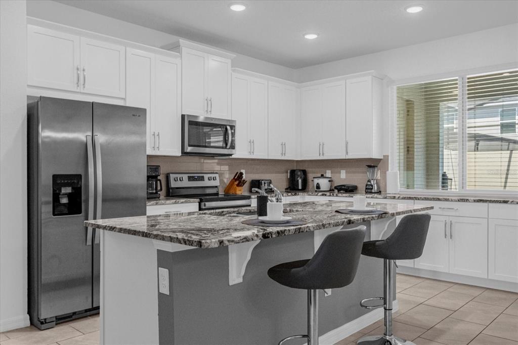 A modern kitchen features white cabinets, granite countertops, a center island, and stainless steel appliances — 1644 TROPICAL PALMS CIRCLE, KISSIMMEE, FL