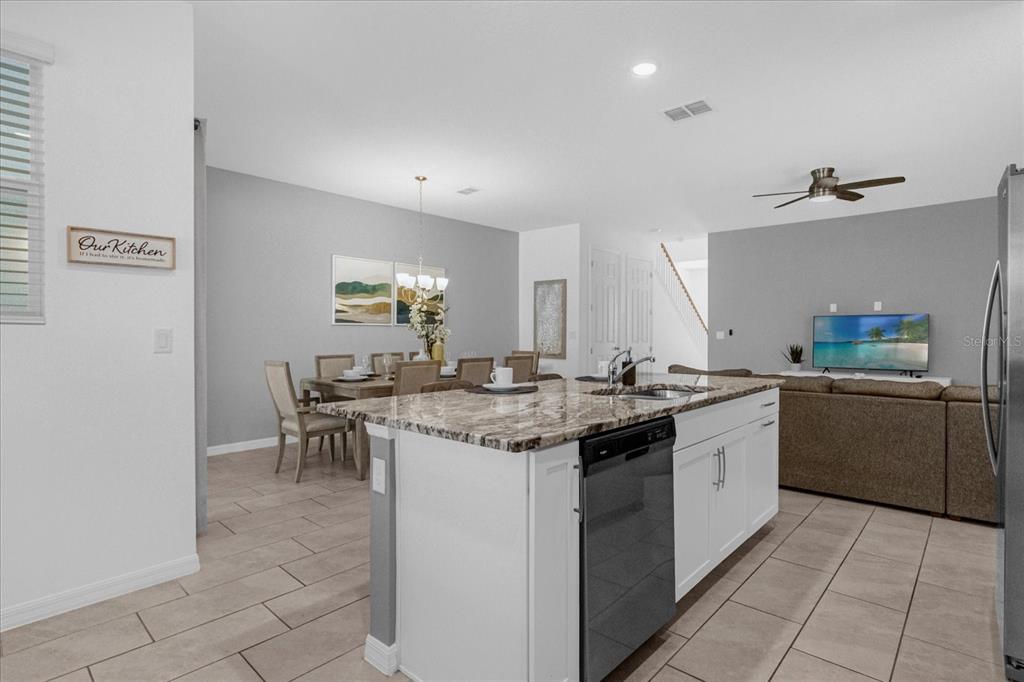 A kitchen island with a granite countertop sits in front of a dining area and living room — 1644 TROPICAL PALMS CIRCLE, KISSIMMEE, FL