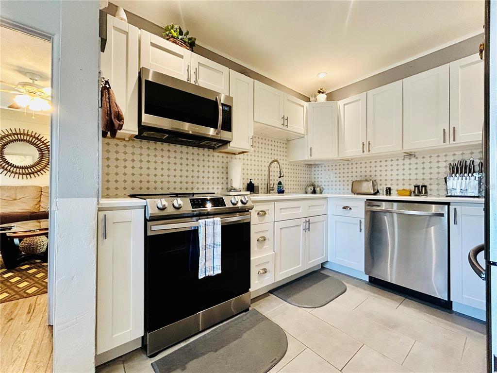 A kitchen with white cabinets, stainless steel appliances, and a patterned tile backsplash — 6190 6TH STREET S, ST PETERSBURG, FL
