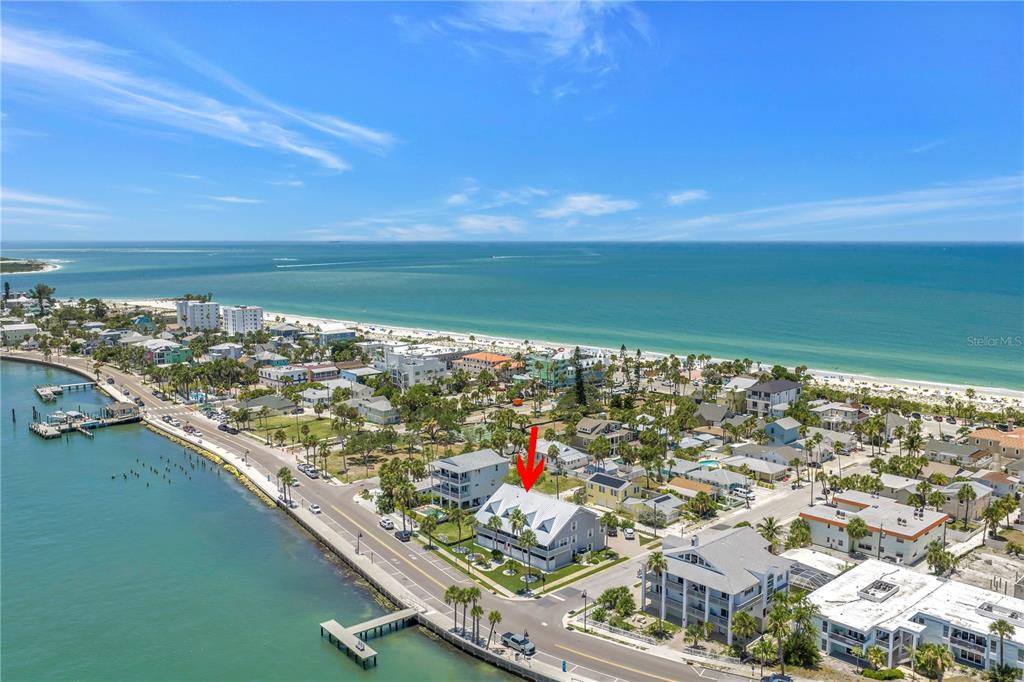 An aerial view shows a multi-story coastal home near a beach and a bay — 1010 PASS A GRILLE WAY UNIT 2, ST PETE BEACH, FL