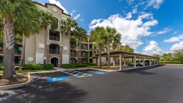 An exterior view of a multi-story apartment building with a covered parking area and palm trees — 16706 VARDON TERRACE UNIT 303, BRADENTON, FL