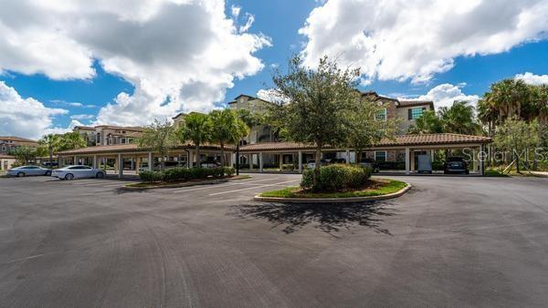 A parking lot with covered carports sits in front of a multi-story apartment building — 16706 VARDON TERRACE UNIT 303, BRADENTON, FL