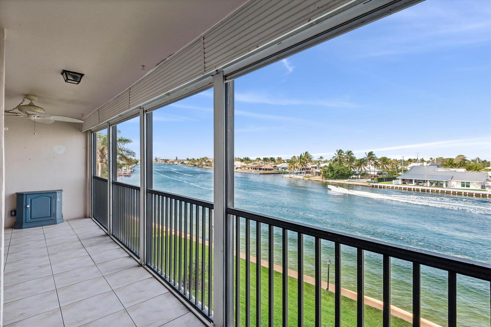 A screened-in balcony with tile flooring overlooks a canal with a boat passing by — 985 SE 19TH Avenue # 303, Deerfield Beach FL 33441, DEERFIELD BEACH, FL
