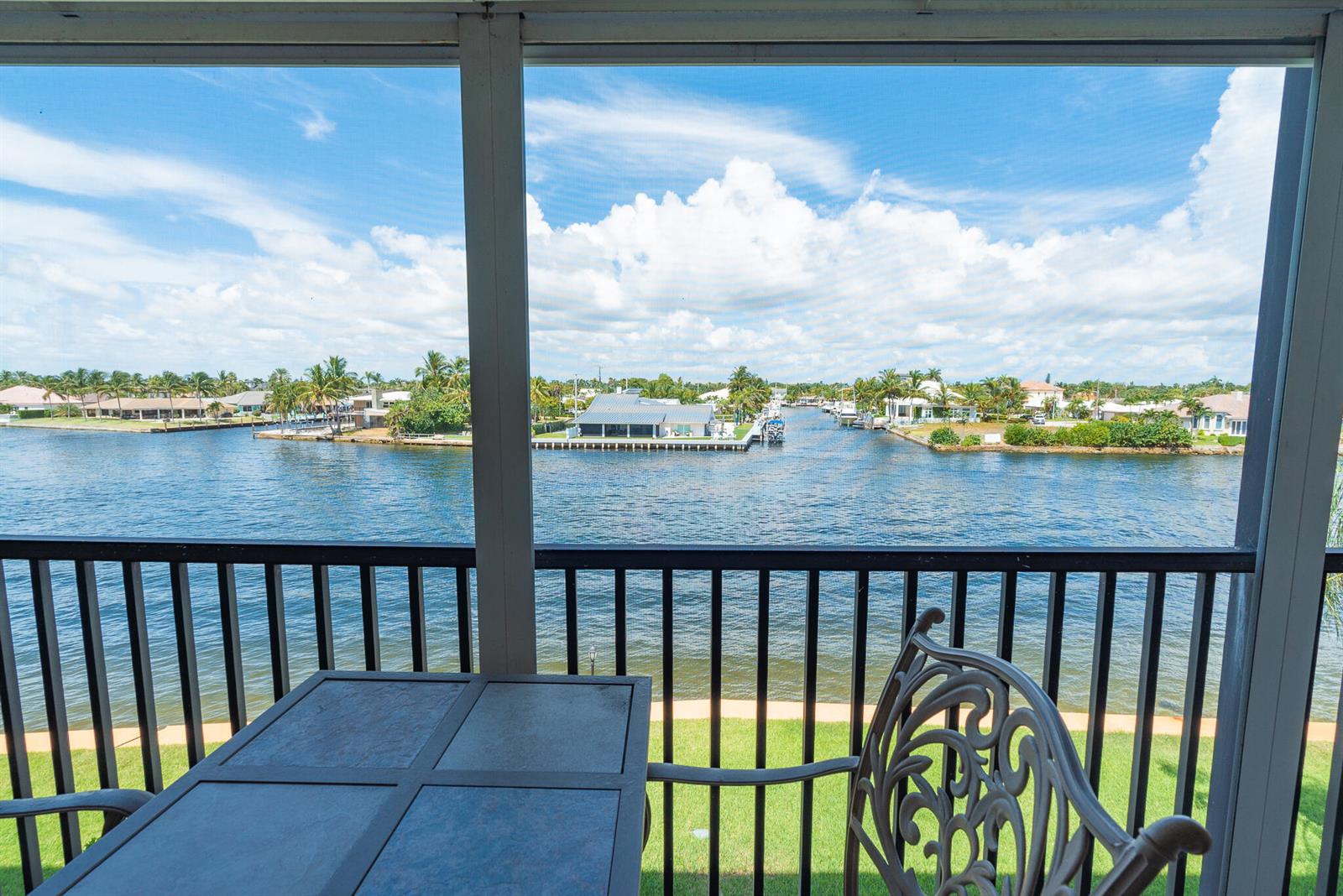 A screened-in balcony overlooks a canal with houses and palm trees in the distance — 985 SE 19TH Avenue # 303, Deerfield Beach FL 33441, DEERFIELD BEACH, FL