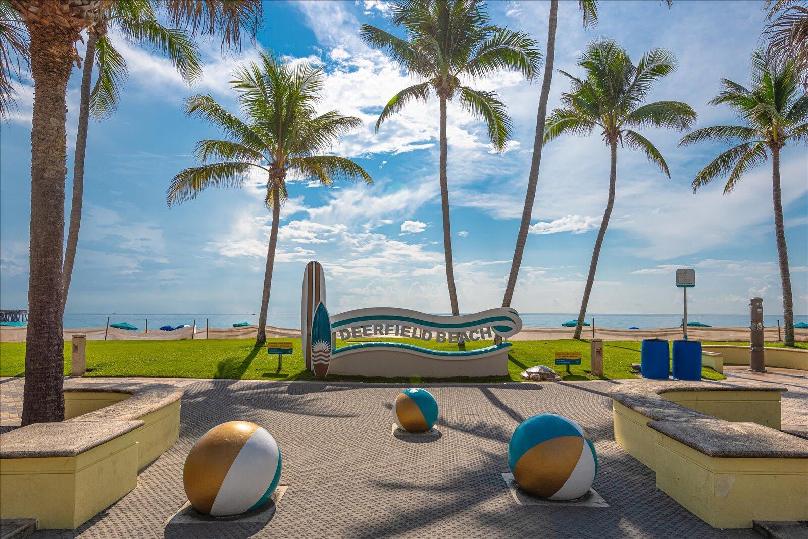 A Deerfield Beach sign stands on a paved plaza with palm trees and the ocean — 985 SE 19TH Avenue # 303, Deerfield Beach FL 33441, DEERFIELD BEACH, FL