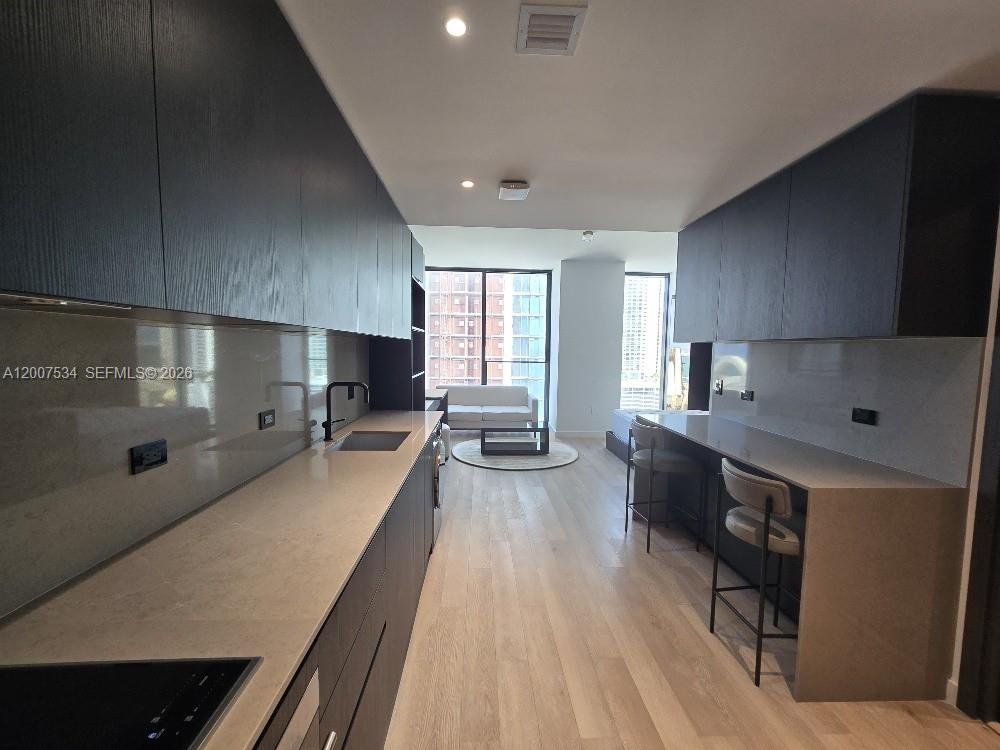 A modern kitchen with dark cabinetry and a breakfast bar overlooks a living area — 20 NE NE 11 Street # 2307, Miami FL 33132, MIAMI, FL
