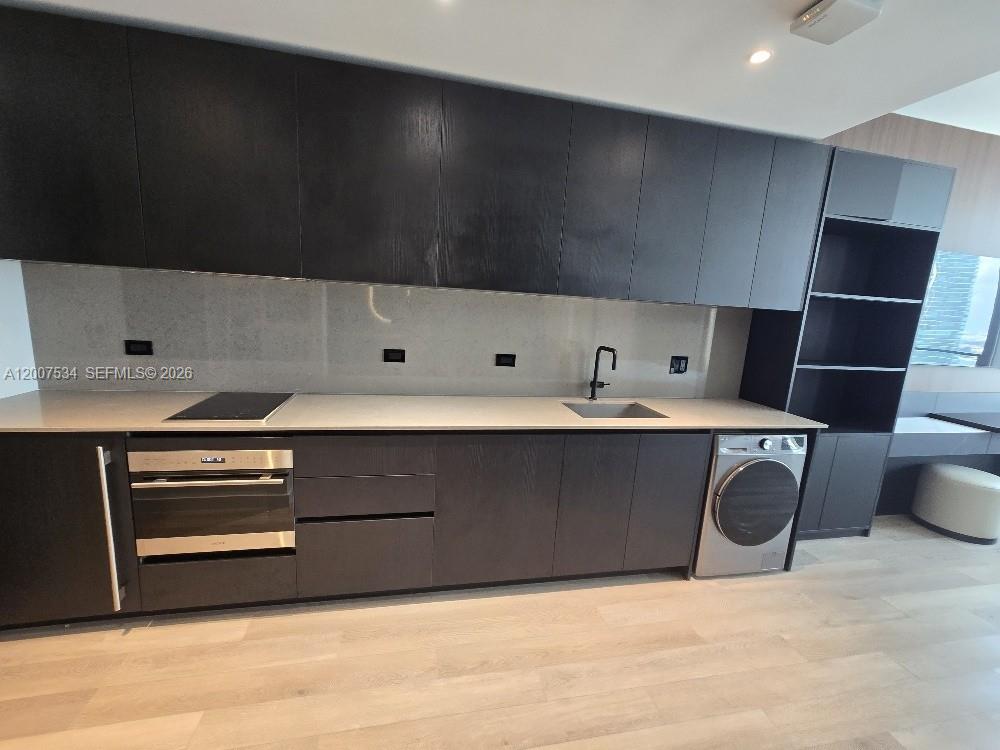 A modern kitchen features dark cabinetry, light countertops, a built-in oven, and a washing machine — 20 NE NE 11 Street # 2307, Miami FL 33132, MIAMI, FL