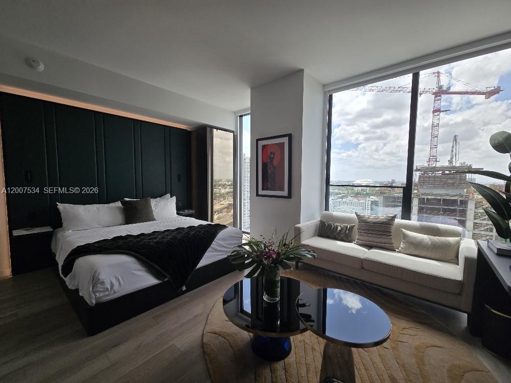 A modern bedroom features a dark paneled wall, a bed, seating, and city construction views — 20 NE NE 11 Street # 2307, Miami FL 33132, MIAMI, FL