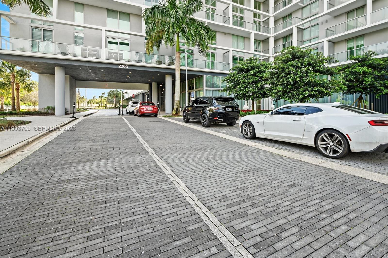 A paved driveway leads to the entrance of a modern multi-story apartment building — 2000 Metropica Way # 508, Sunrise FL 33323, SUNRISE, FL