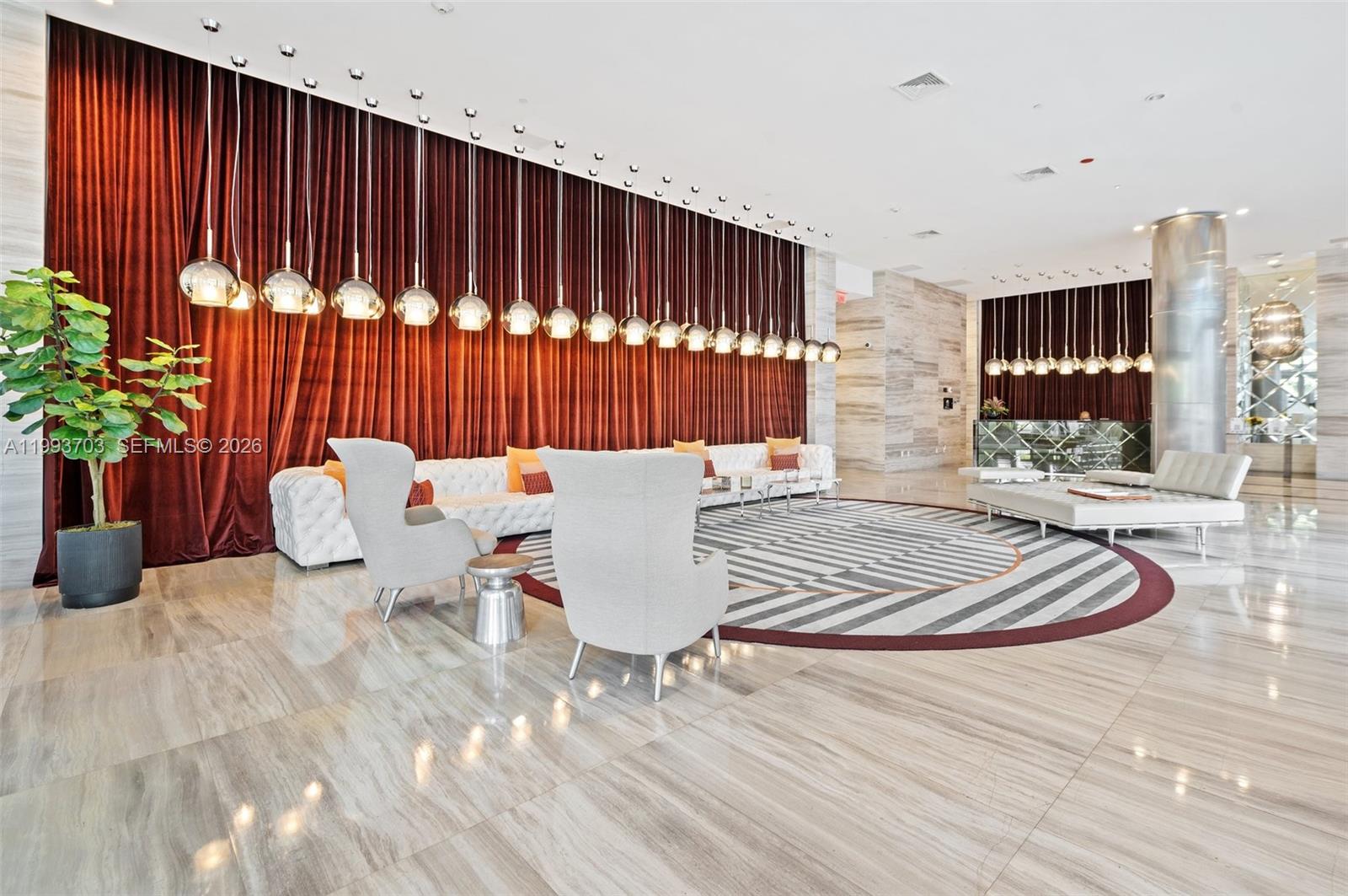 A modern lobby features a long velvet curtain, circular rug, and rows of pendant lights — 2000 Metropica Way # 508, Sunrise FL 33323, SUNRISE, FL