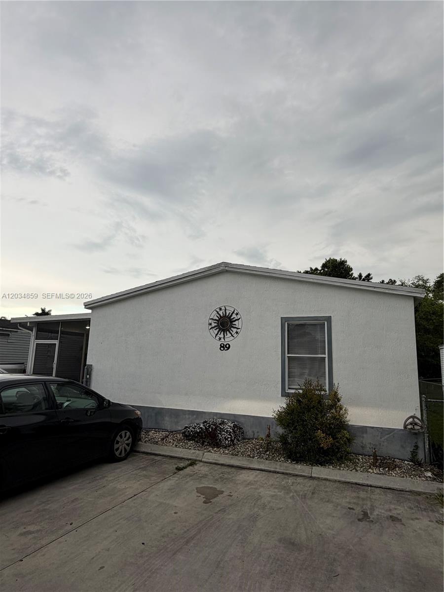 A white single-story house exterior features a sun-shaped wall decoration and a black car parked — 19800 SW 180th Ave, Miami FL 33187, MIAMI, FL