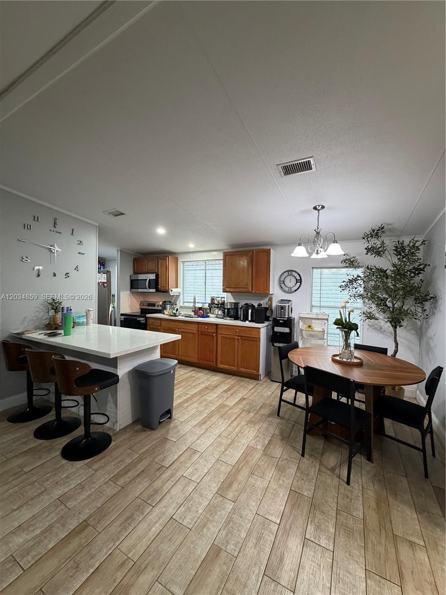 A kitchen and dining area features wood cabinets, a white island, and wood-look tile flooring — 19800 SW 180th Ave, Miami FL 33187, MIAMI, FL