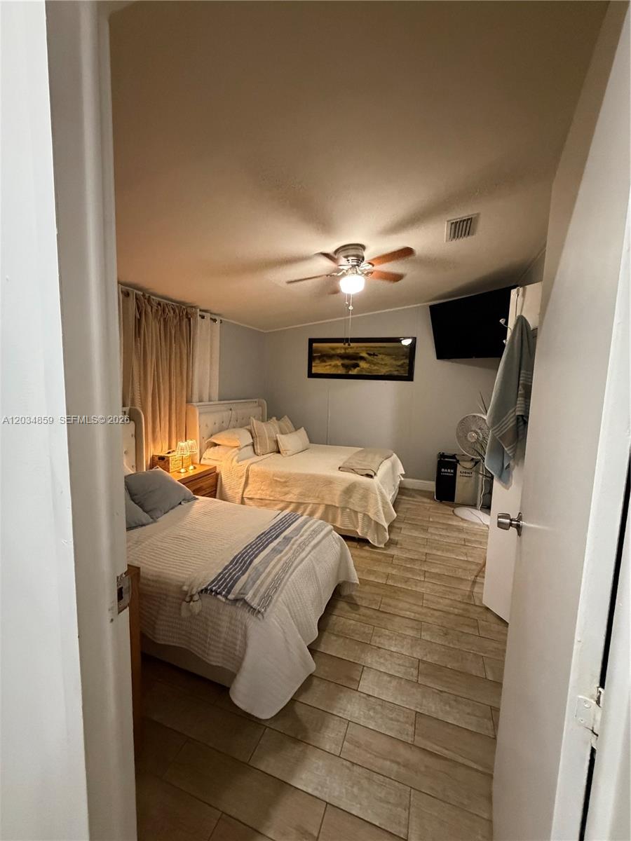 A bedroom features two beds, light-colored wood-look tile flooring, and a ceiling fan — 19800 SW 180th Ave, Miami FL 33187, MIAMI, FL