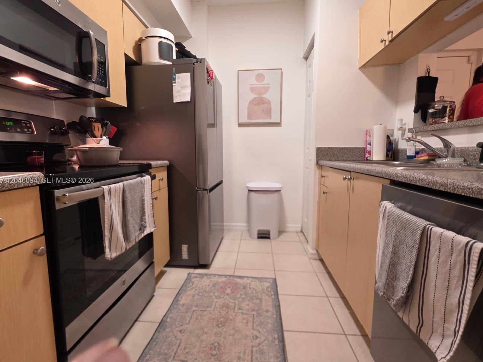 A galley kitchen features light wood cabinets, stainless steel appliances, and a patterned area rug — 2201 W Preserve Way # 208, Miramar FL 33025, MIRAMAR, FL