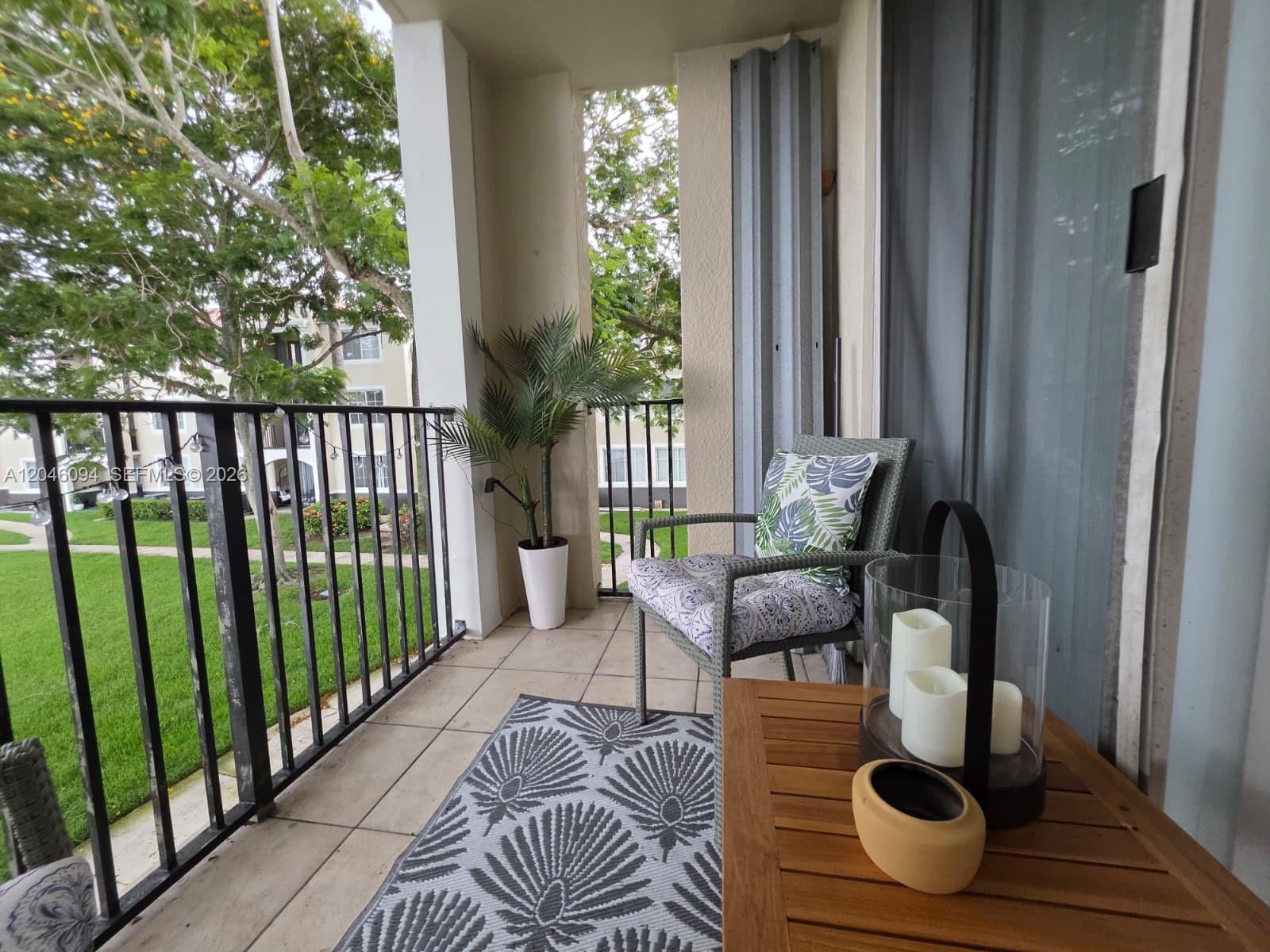 A covered balcony features tile flooring, a patterned rug, a wicker chair, and a table — 2201 W Preserve Way # 208, Miramar FL 33025, MIRAMAR, FL