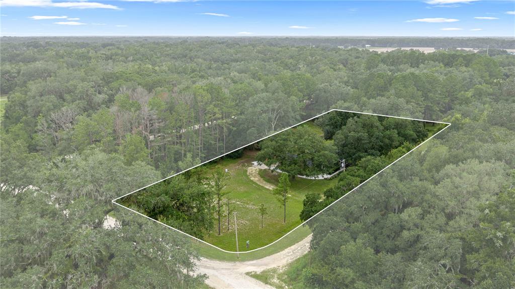 An aerial view shows a house nestled among trees on a large, partially cleared lot — 13750 105 PLACE SW, DUNNELLON, FL