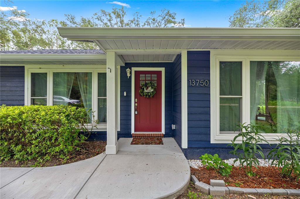 A blue house exterior features a red front door, white trim, and a concrete walkway — 13750 105 PLACE SW, DUNNELLON, FL