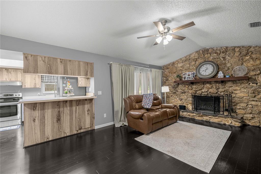 A living room with dark wood floors, a stone fireplace, and an adjacent kitchen area — 13750 105 PLACE SW, DUNNELLON, FL