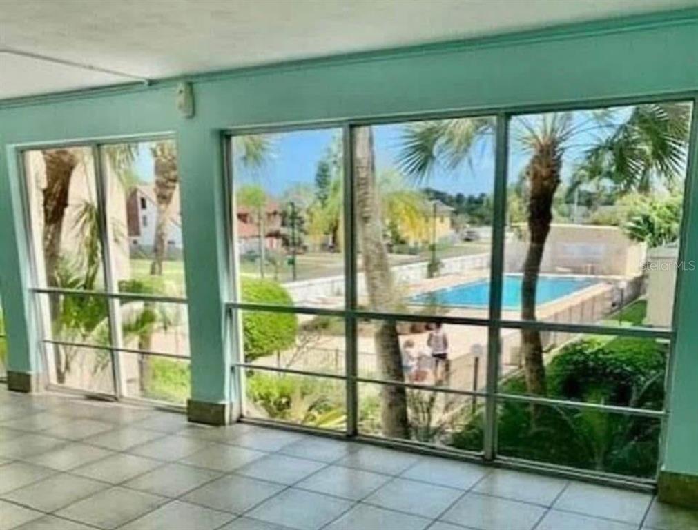 A tiled sunroom features large windows overlooking a swimming pool and palm trees — 223 COLUMBIA DRIVE UNIT 211, CAPE CANAVERAL, FL