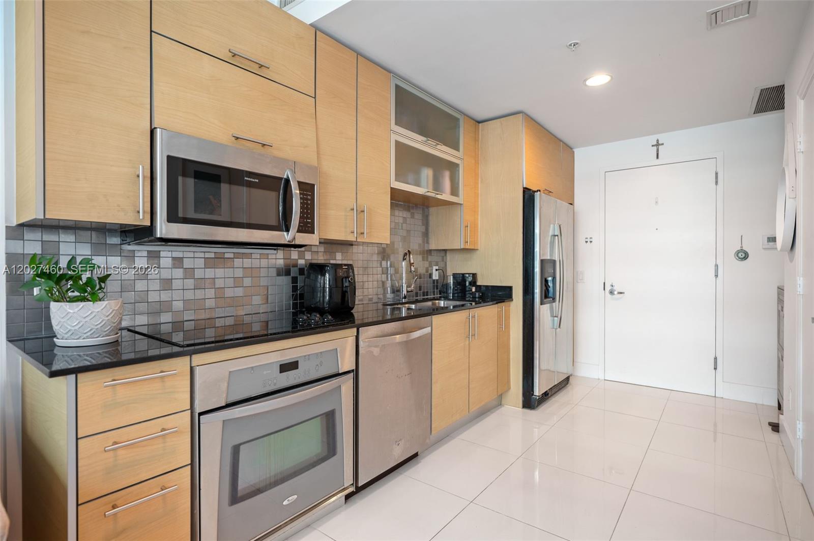 A modern kitchen features light wood cabinets, stainless steel appliances, and a dark tiled backsplash — 60 SW 13th St # 4408, Miami FL 33130, MIAMI, FL