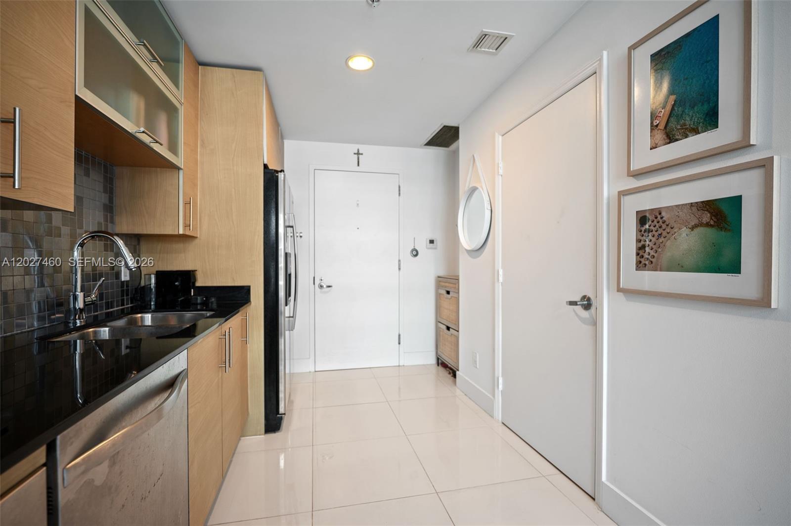 A kitchen features light wood cabinets, black countertops, stainless steel appliances, and white tile flooring — 60 SW 13th St # 4408, Miami FL 33130, MIAMI, FL