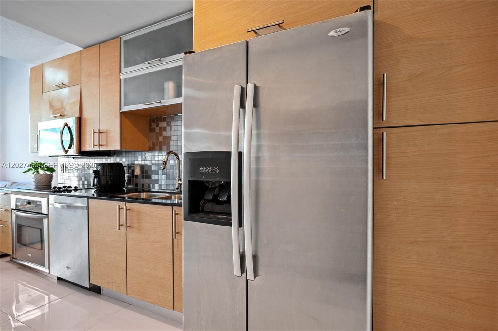 A modern kitchen features light wood cabinetry, stainless steel appliances, and a tiled backsplash — 60 SW 13th St # 4408, Miami FL 33130, MIAMI, FL