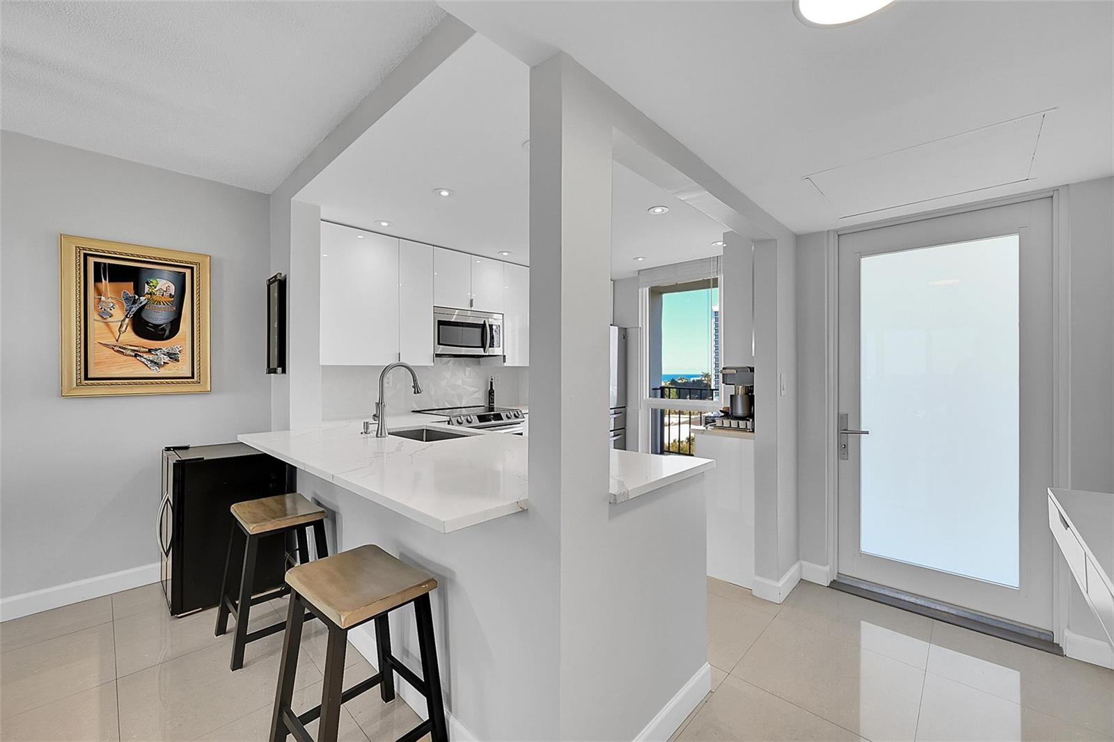 A modern kitchen features white cabinets, quartz countertops, a breakfast bar, and a glass door — 521 N Riverside Drive # 707, Pompano Beach FL 33062, POMPANO BEACH, FL