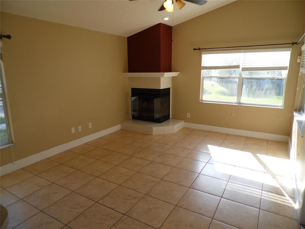 An empty living room features tan tile floors, beige walls, and a corner fireplace — 11020 FELTON COURT, ORLANDO, FL