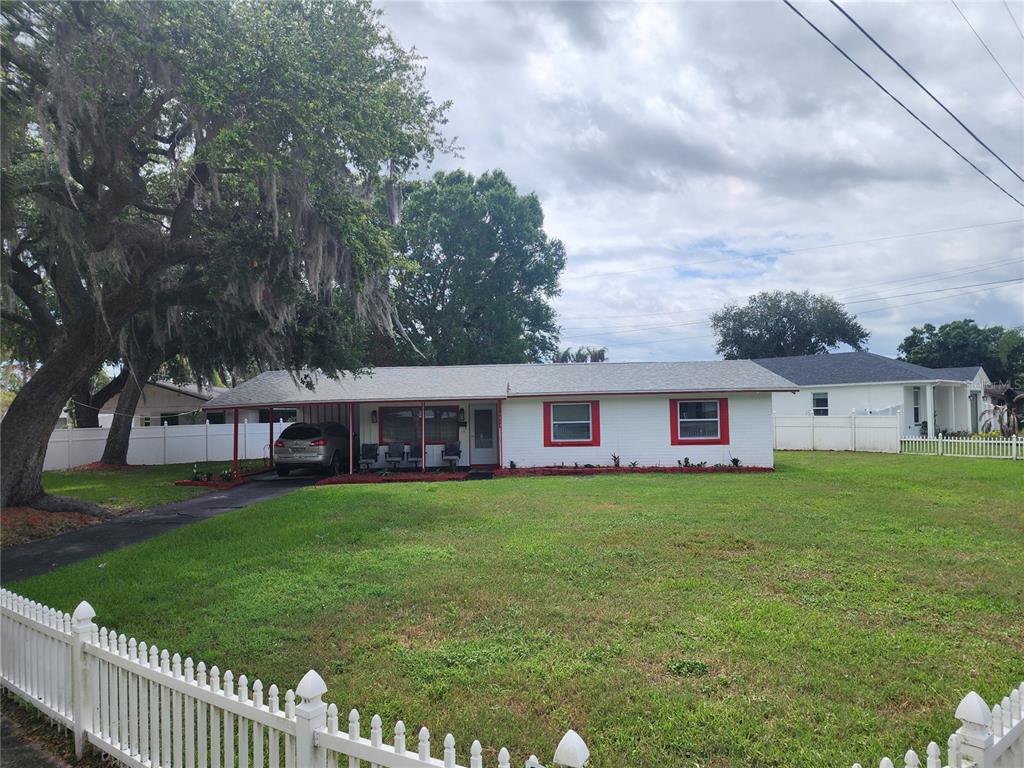 A single-story white house with a red-trimmed carport and windows sits behind a white fence — 1317 MOSS LANE, COCOA, FL