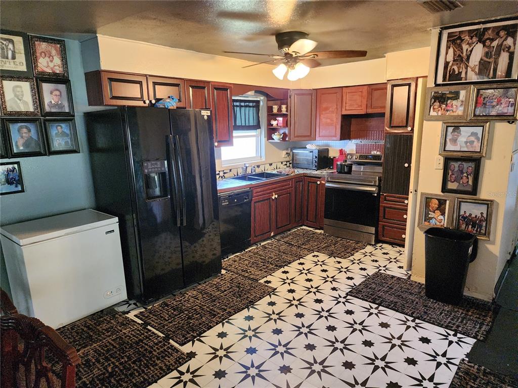 A kitchen features dark wood cabinets, black appliances, and a patterned black and white floor — 1317 MOSS LANE, COCOA, FL